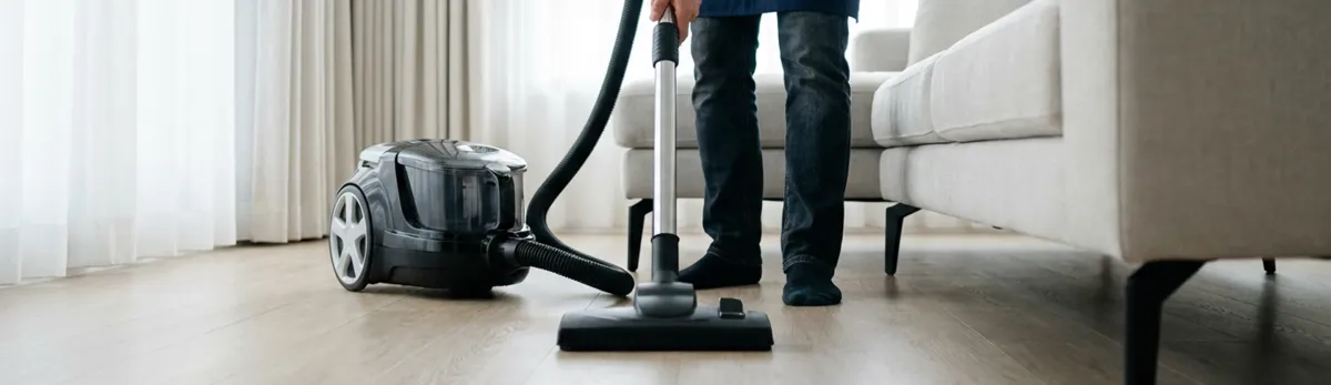Professional house cleaner vacuuming a living room floor with a canister vacuum cleaner, Sacramento, CA.